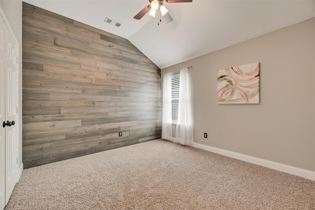 carpeted empty room featuring ceiling fan, wood walls, vaulted ceiling, and baseboards
