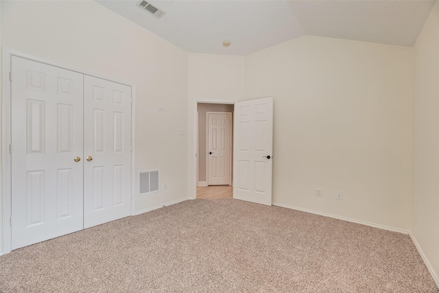 unfurnished bedroom with light colored carpet, vaulted ceiling, a closet, and baseboards