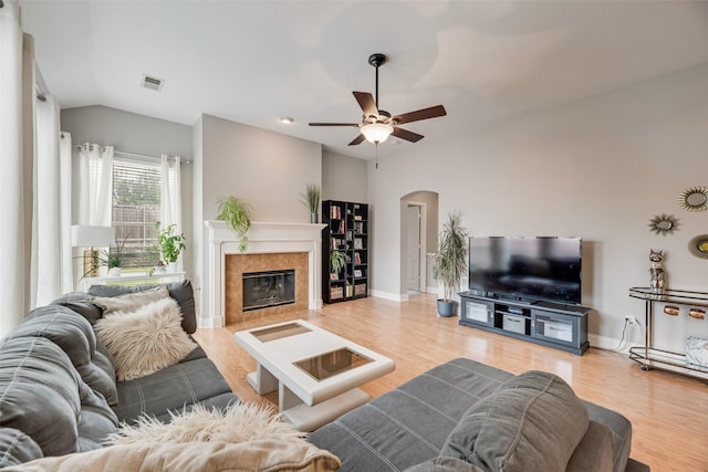 living room with arched walkways, wood finished floors, a tiled fireplace, vaulted ceiling, and ceiling fan
