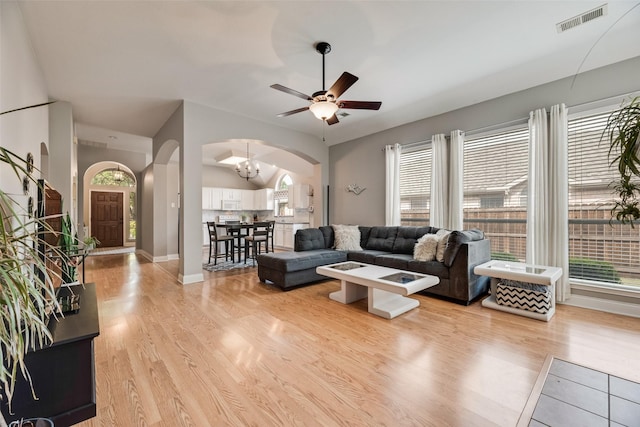 living room featuring arched walkways, light wood-style flooring, a chandelier, and a ceiling fan