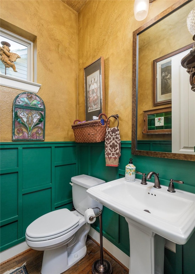 bathroom with wood finished floors, a decorative wall, toilet, a textured wall, and wainscoting