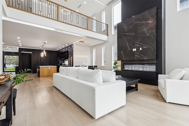 living area featuring light wood-style floors, a premium fireplace, a towering ceiling, and recessed lighting