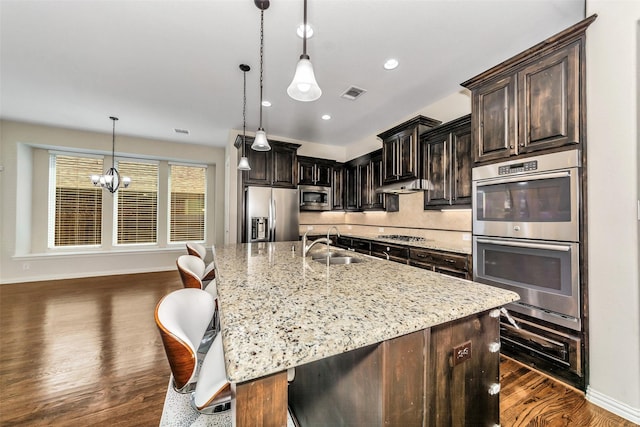 5112 Fringetree Dr, Mckinney, TX 75071 - kitchen with stainless steel appliances, a sink, dark wood finished floors, light stone counters, and a center island with sink