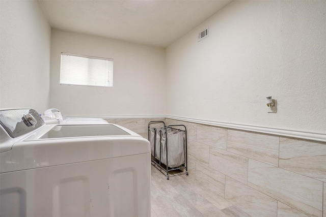 3554 Cromart Ct N, Fort Worth, TX 76133 - laundry room featuring washing machine and dryer, tile walls, wainscoting, and light wood-style floors