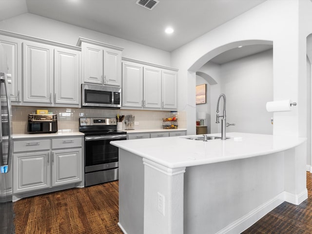 kitchen with appliances with stainless steel finishes, a sink, arched walkways, backsplash, and light countertops