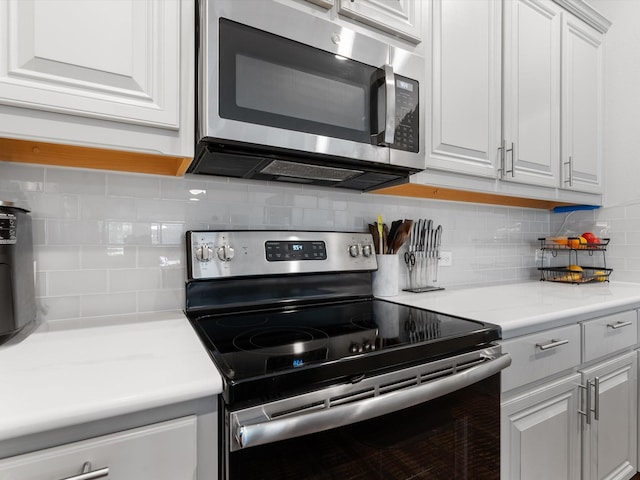 kitchen with appliances with stainless steel finishes, backsplash, light countertops, and white cabinets