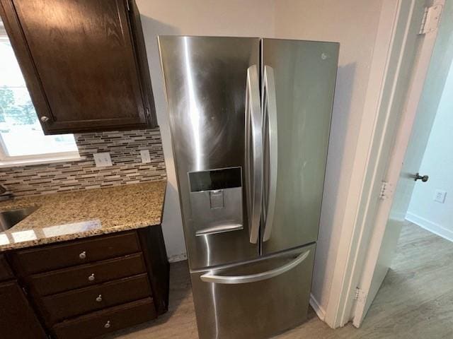 kitchen view of stainless steel fridge with ice dispenser, dark brown cabinetry, tasteful backsplash, light stone countertops, and light wood-style floors