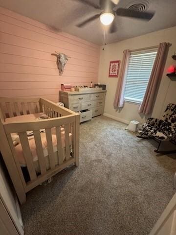 261 Barker St, Stephenville, TX 76401 - bedroom with wood walls, light carpet, a crib, and ceiling fan