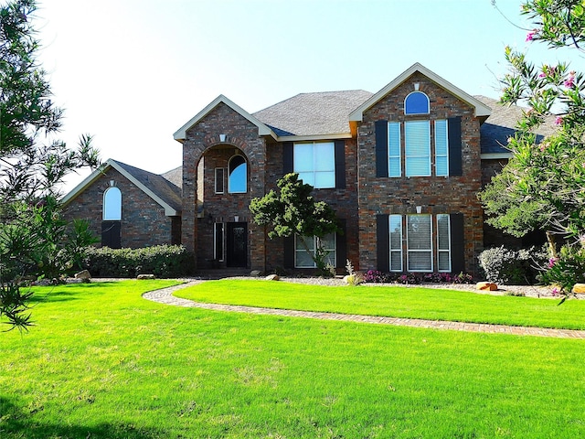 traditional-style home featuring a front yard, roof with shingles, and brick siding