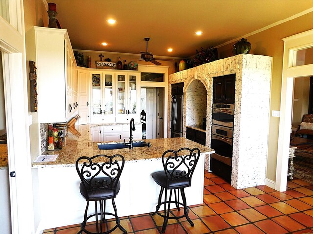 kitchen featuring freestanding refrigerator, a peninsula, a sink, crown molding, and a ceiling fan