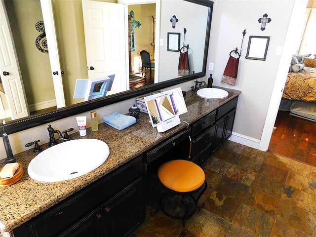 bathroom with baseboards, stone tile floors, and double vanity