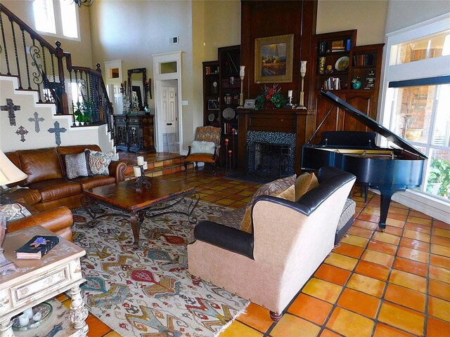 tiled living area featuring healthy amount of natural light, a towering ceiling, stairs, and a fireplace with flush hearth
