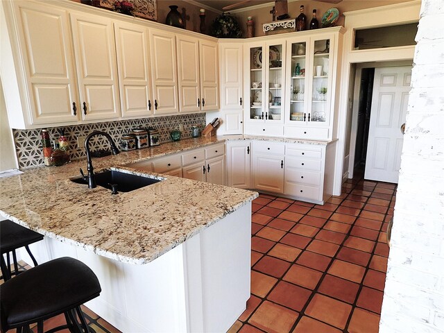 kitchen featuring a sink, a peninsula, white cabinets, backsplash, and glass insert cabinets