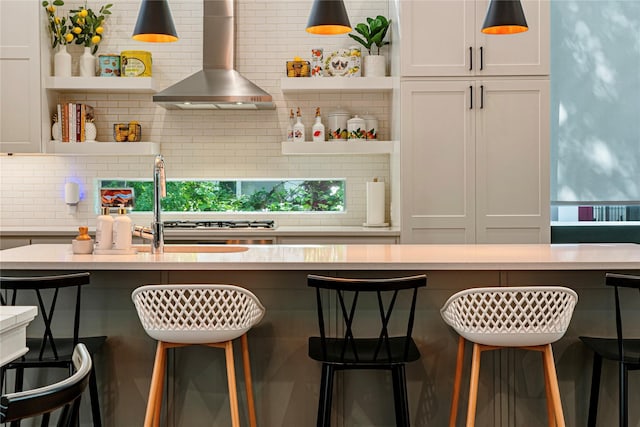 bar featuring wall chimney exhaust hood, decorative backsplash, and hanging light fixtures