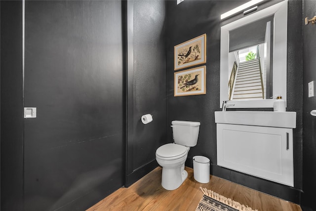 half bath with wood finished floors, toilet, and vanity