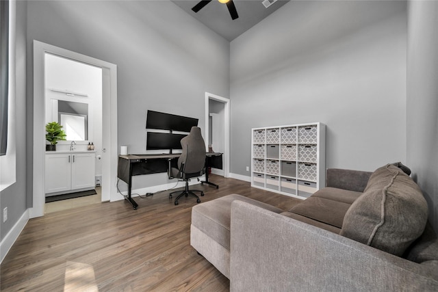 office space featuring ceiling fan, wood finished floors, a high ceiling, and baseboards