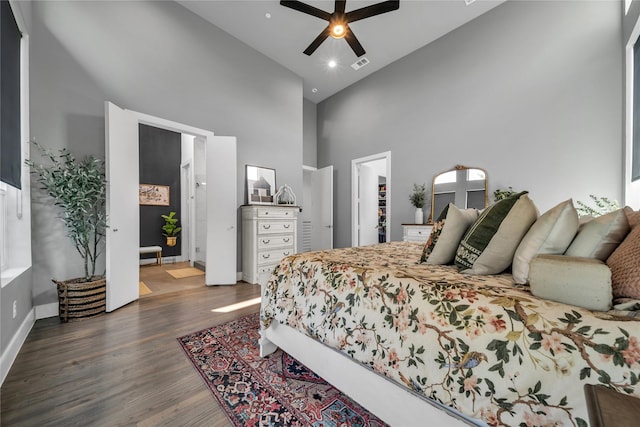 bedroom with a high ceiling, wood finished floors, baseboards, ceiling fan, and a walk in closet