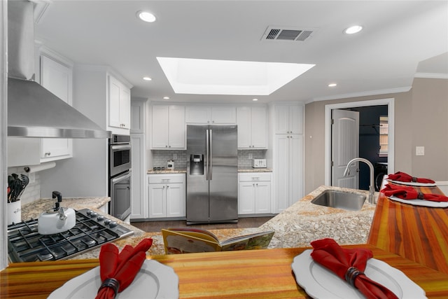 7610 Bantry Cir, Dallas, TX 75248 - kitchen featuring appliances with stainless steel finishes, a sink, wall chimney range hood, a skylight, and tasteful backsplash