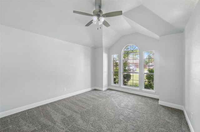 carpeted empty room with vaulted ceiling, a ceiling fan, and baseboards