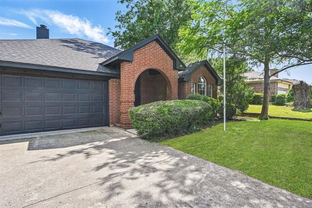 view of front of home with brick siding, driveway, a front yard, a chimney, and a garage