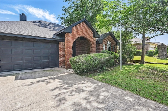 view of front of property with brick siding, driveway, a chimney, an attached garage, and a front yard