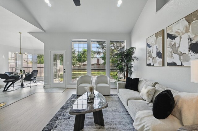 living room featuring healthy amount of natural light, wood finished floors, a chandelier, and high vaulted ceiling