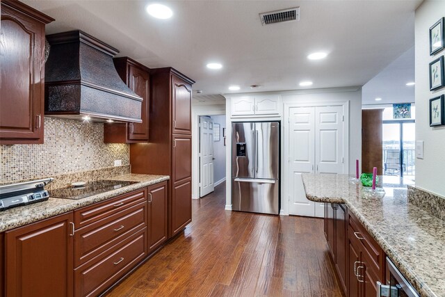 kitchen with stainless steel fridge, dark wood-style floors, tasteful backsplash, custom range hood, and light stone counters