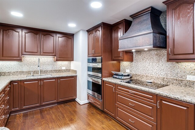 kitchen featuring a sink, custom exhaust hood, stainless steel double oven, black electric stovetop, and dark wood-style floors