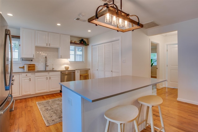 1205 Ranier St, Dallas, TX 75208 - kitchen with a sink, light wood-style floors, white cabinetry, a breakfast bar, and appliances with stainless steel finishes