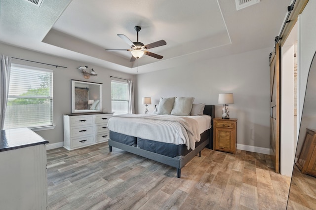 2607 Austin Dr, Granbury, TX 76048 - bedroom featuring a barn door, a tray ceiling, baseboards, and light wood-type flooring