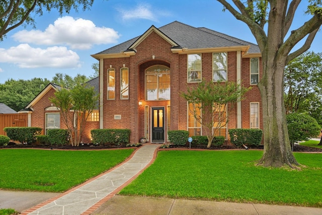 traditional-style home featuring brick siding, a front yard, and a shingled roof