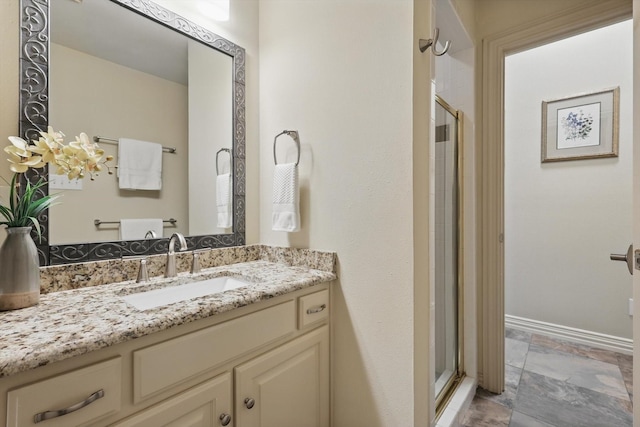 full bath featuring a shower stall, stone finish floors, baseboards, and vanity