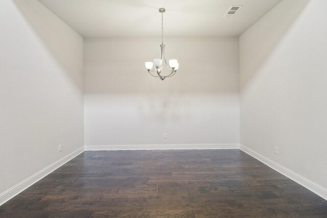empty room featuring a chandelier, dark wood finished floors, and baseboards