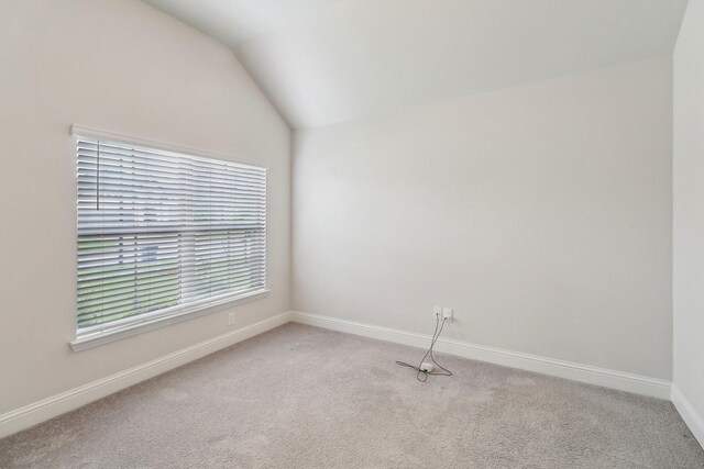 carpeted empty room featuring vaulted ceiling and baseboards