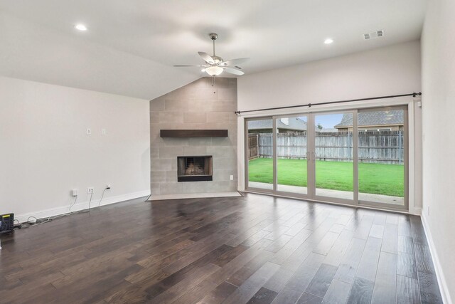 unfurnished living room with a ceiling fan, vaulted ceiling, wood finished floors, a tiled fireplace, and baseboards