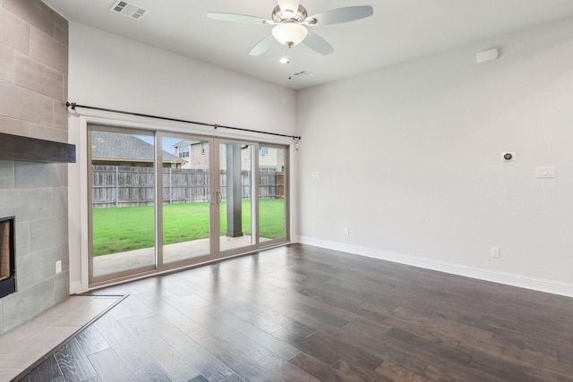 unfurnished living room featuring dark wood-style flooring, a ceiling fan, a tile fireplace, and baseboards