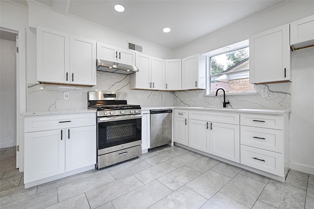 kitchen with appliances with stainless steel finishes, under cabinet range hood, a sink, white cabinets, and decorative backsplash