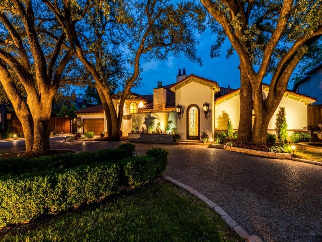 mediterranean / spanish-style house featuring stucco siding, a chimney, concrete driveway, an attached garage, and fence