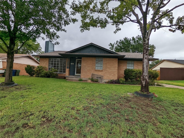 ranch-style home featuring brick siding, a chimney, and a front yard