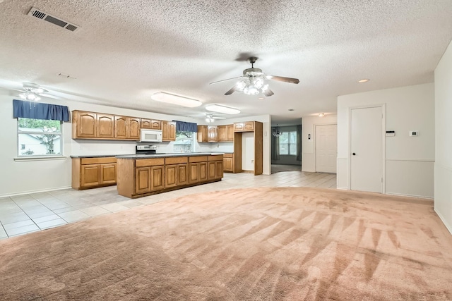 107 San Medina Ln, Joshua, TX 76058 - kitchen featuring white microwave, a ceiling fan, light tile patterned floors, light colored carpet, and brown cabinetry