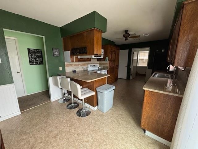 2220 N Clements St, Gainesville, TX 76240 - kitchen featuring range with electric stovetop, a sink, a ceiling fan, a kitchen breakfast bar, and a peninsula