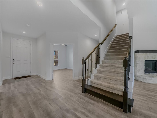 foyer entrance with stairs, a fireplace, wood finished floors, baseboards, and recessed lighting