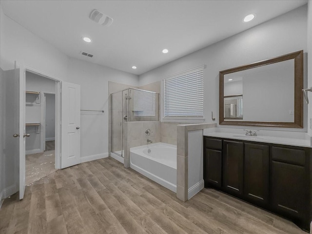 bathroom with a shower stall, a garden tub, wood finished floors, vanity, and recessed lighting