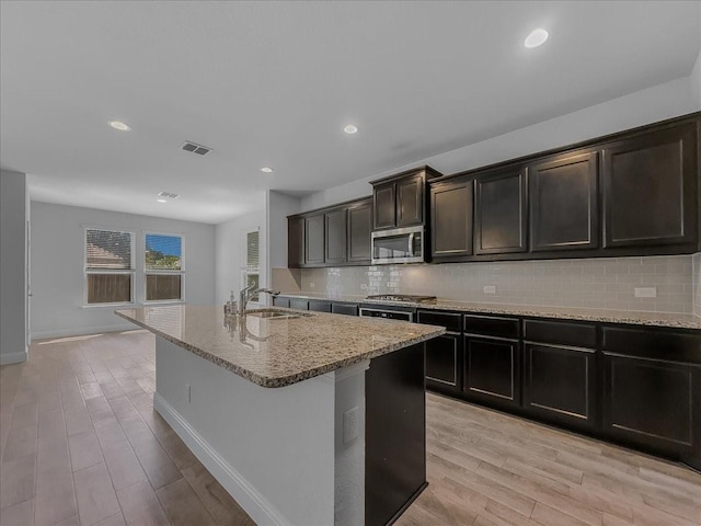 kitchen featuring stainless steel appliances, a sink, light stone counters, light wood-type flooring, and recessed lighting