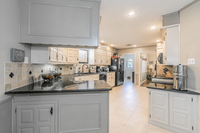 kitchen featuring black appliances, a sink, decorative backsplash, dark stone counters, and a peninsula