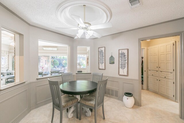dining space with a ceiling fan, a decorative wall, a textured ceiling, ornamental molding, and a wainscoted wall