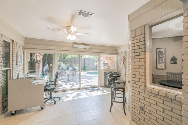 sunroom featuring ceiling fan, tile patterned flooring, and brick wall