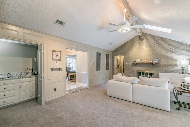 living room featuring brick wall, a ceiling fan, light colored carpet, a skylight, and a fireplace