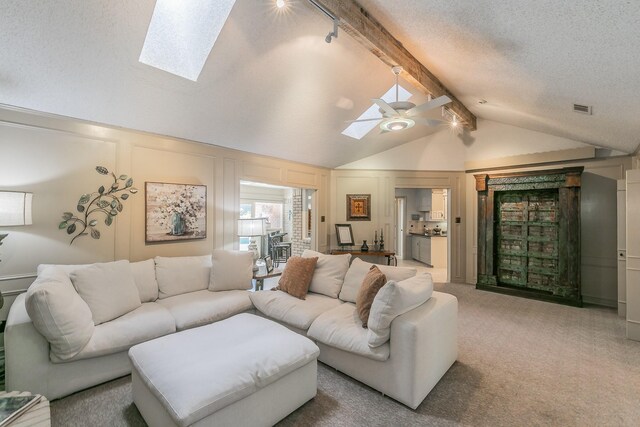 living room featuring a skylight, carpet floors, a ceiling fan, a decorative wall, and a textured ceiling