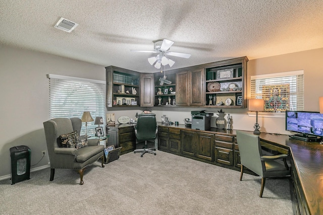 office featuring a ceiling fan, light carpet, built in study area, and a textured ceiling